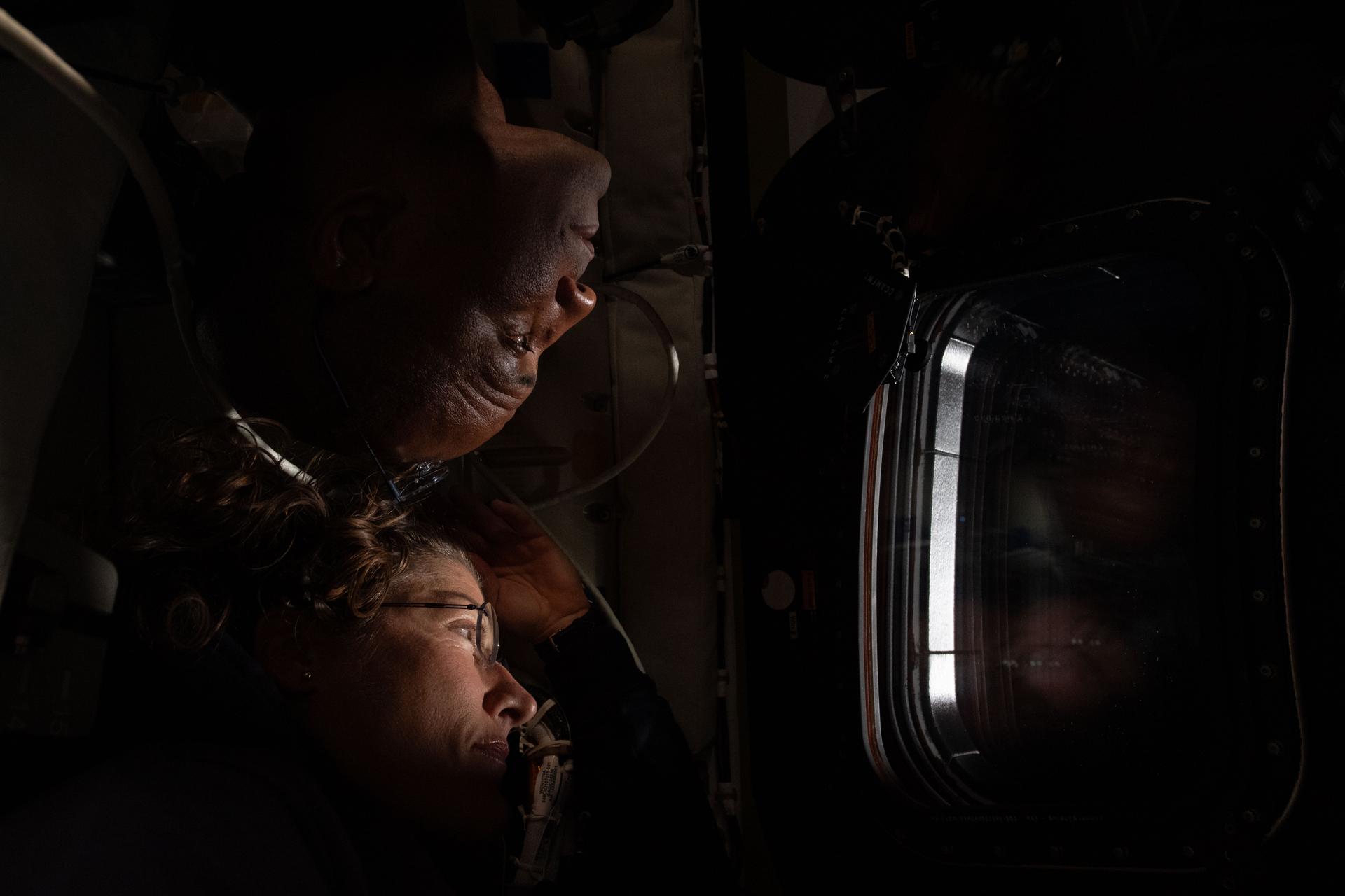 Christina Koch y Victor Glover miran por una ventana de Orion, en penumbra