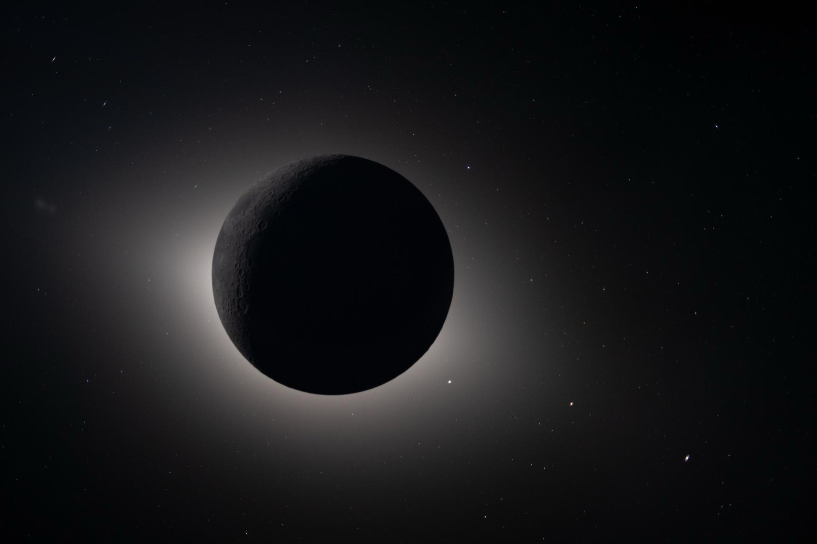 La Luna, negra, tapa el Sol por completo; alrededor, un halo de luz y estrellas