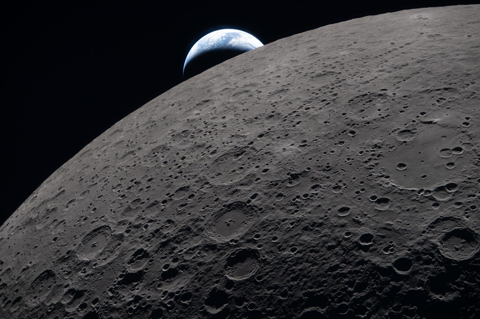 La superficie de la Luna llena la imagen y la Tierra asoma pequeña al fondo